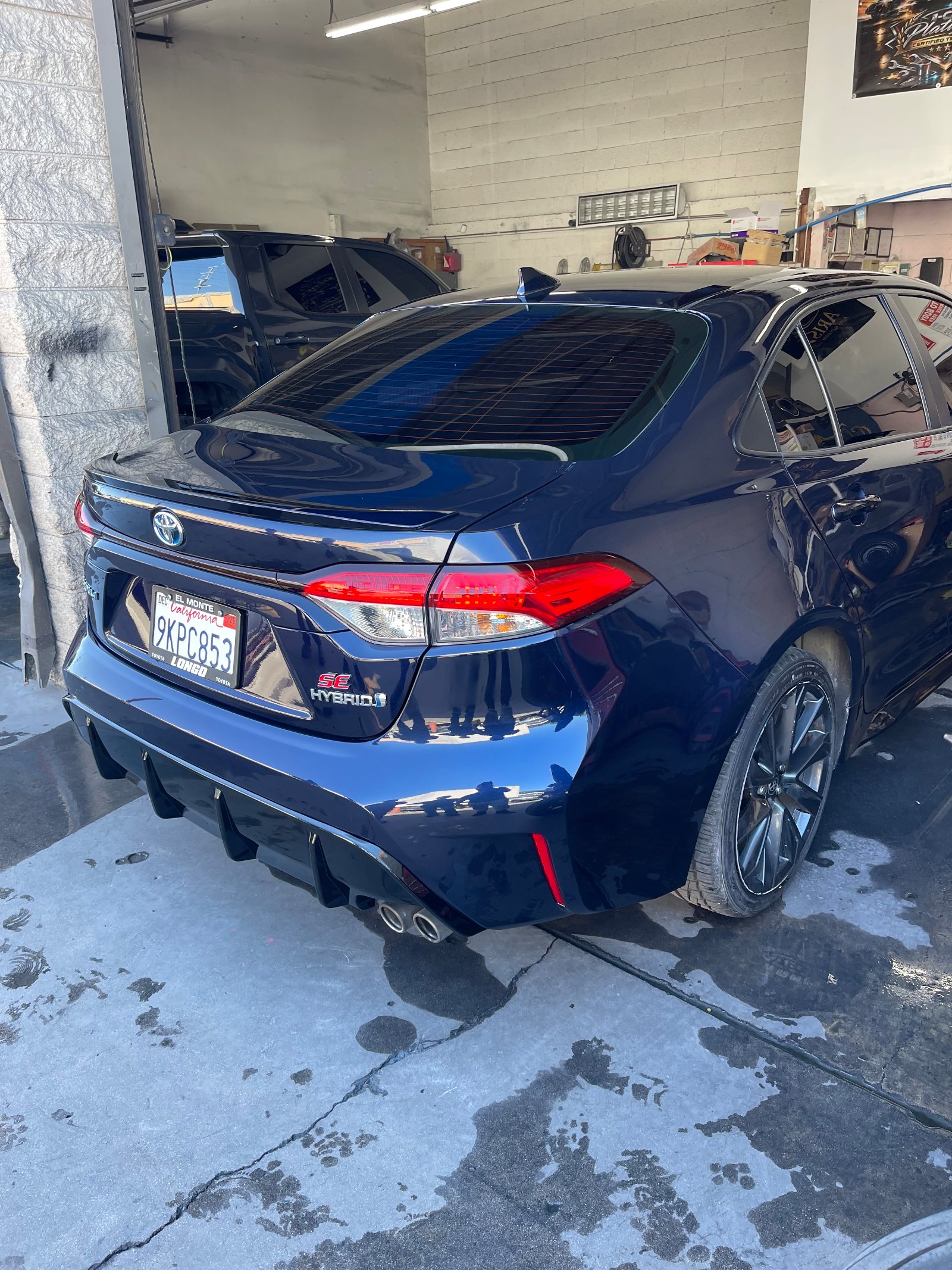 The finished navy Corolla, rear three-quarter, glossy and clean, standing just inside the open roll-up door with daylight